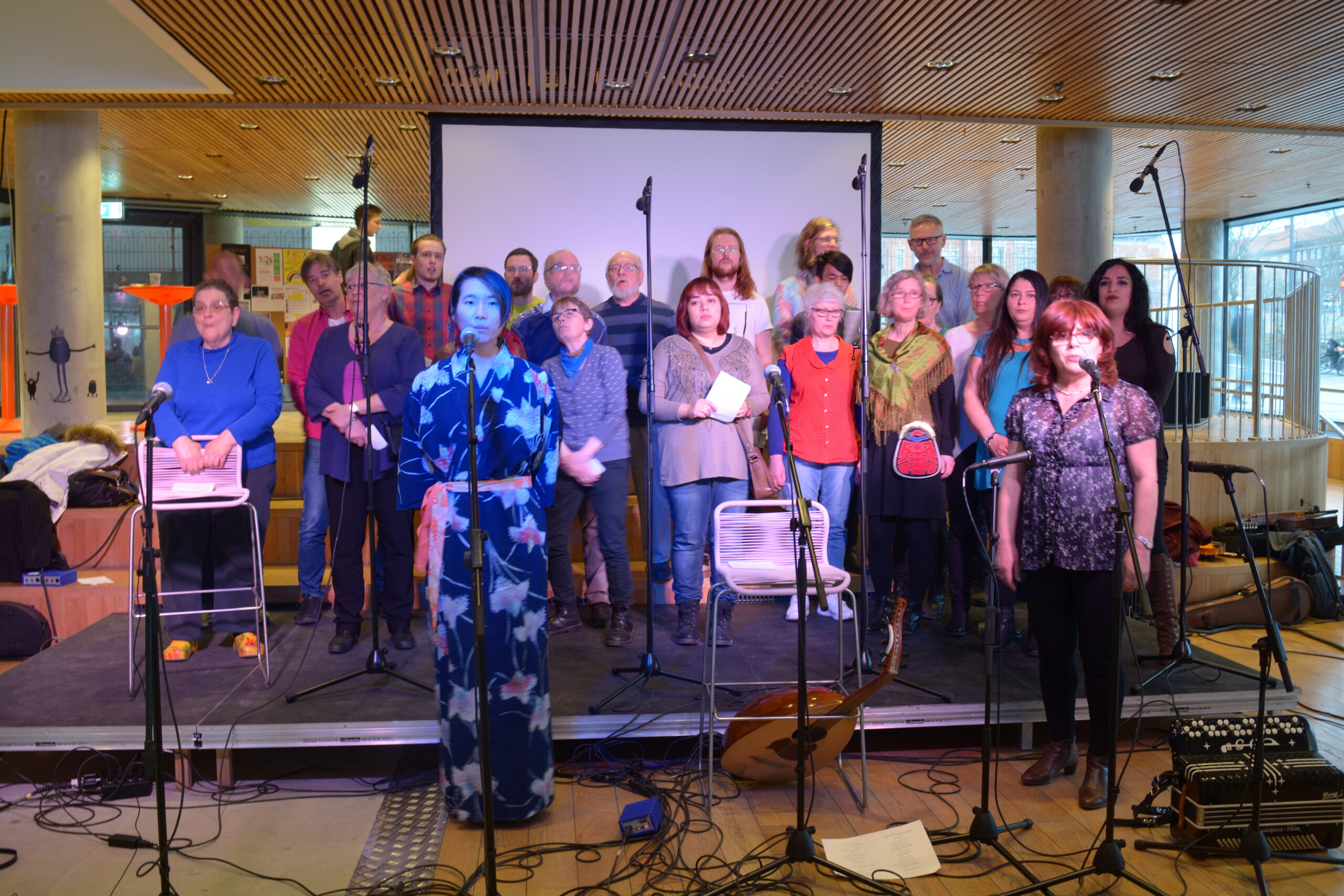 En bild på ca 15 av medlemmarna i Vän i Umeås kör Happy Mix som sjunger på en scen
