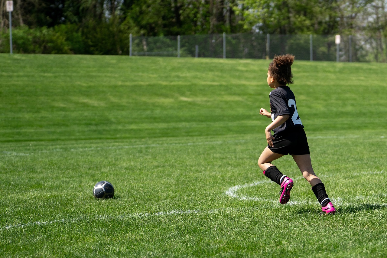 flicka som tar sats för att sparka en fotboll på en grön utomhusplan