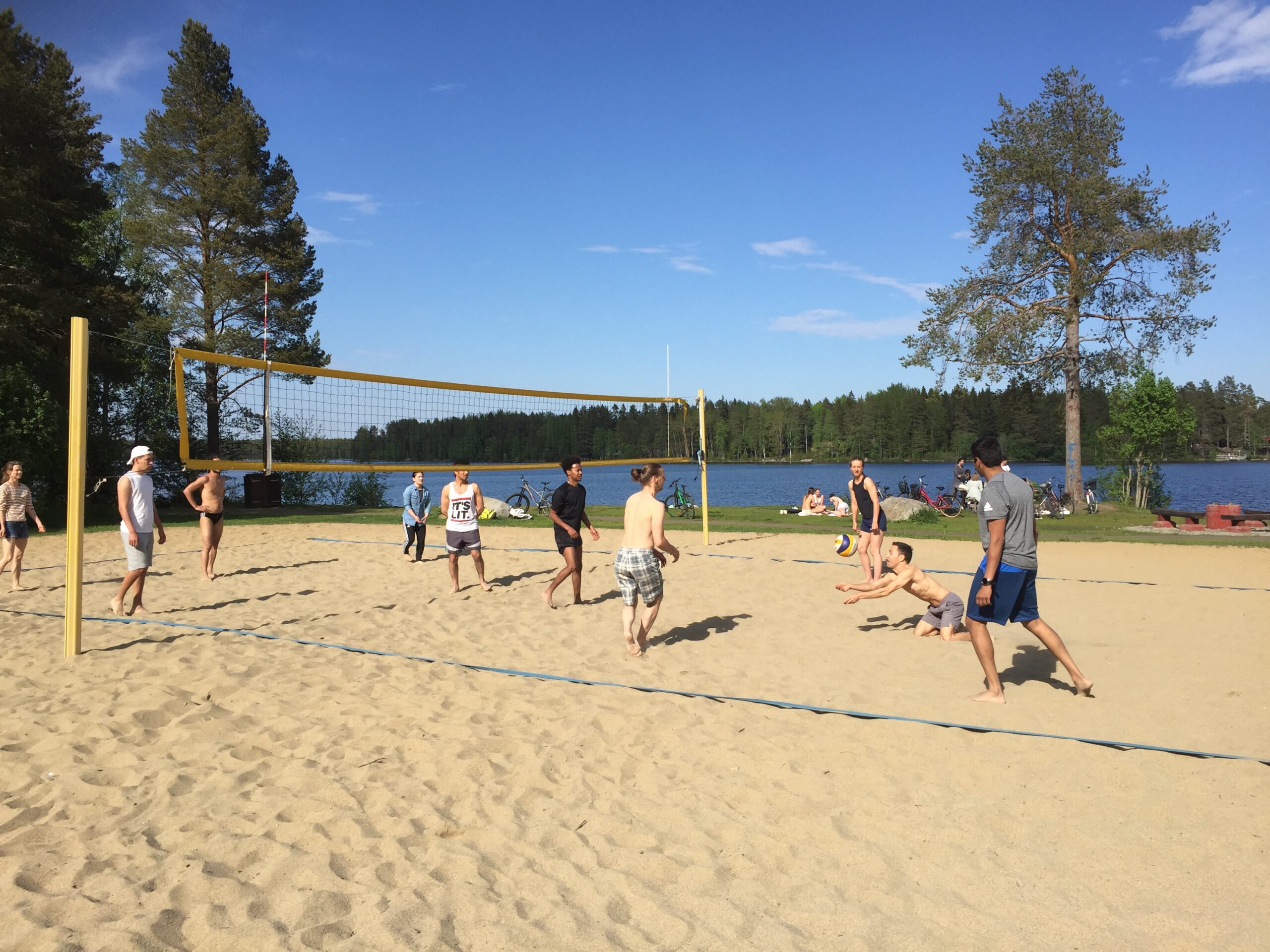 Några ungdomar som spelar beachvolleyboll på en strand vid vatten