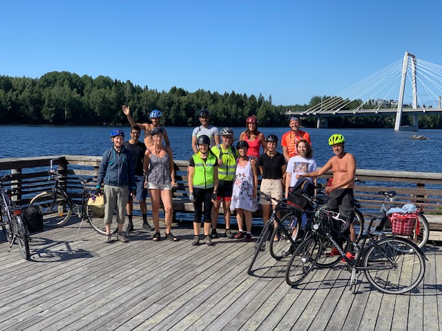 Några glada vänner i Umeå står med cyklar på ett trädäck vid vatten
