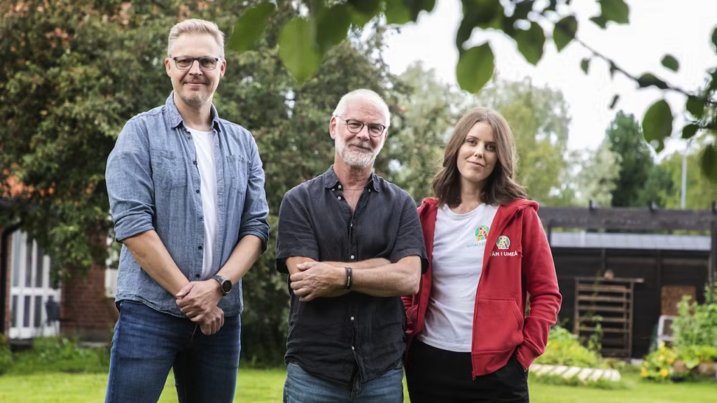 två män och en kvinna står utomhus. Alla tre ser glada ut.