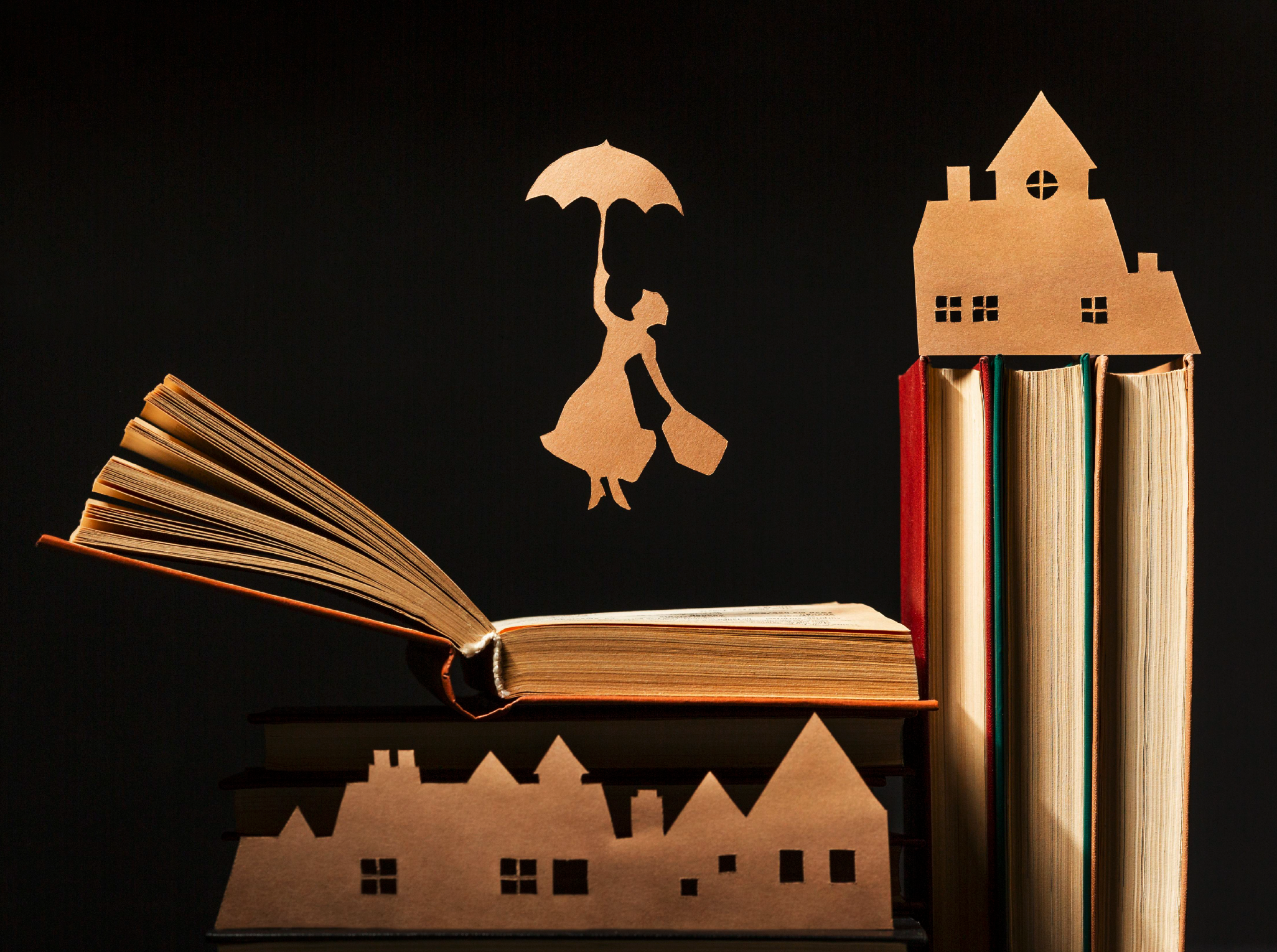 en bild på böcker och en pappersfigur som flyger med sitt paraply och även några pappershussiluetter