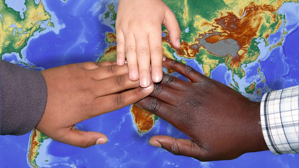 tre händer (en ljushyad, två mörkhyade) som nuddar varandra över en världskarta